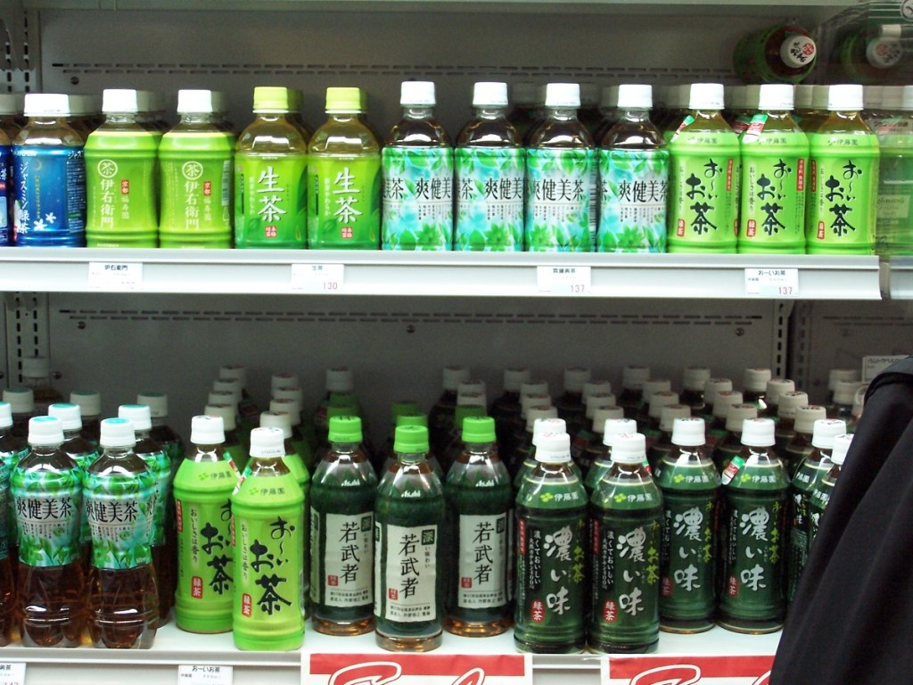 A refrigerator shelf filled with various brands of Japanese green tea bottles at a Haneda Airport convenience store