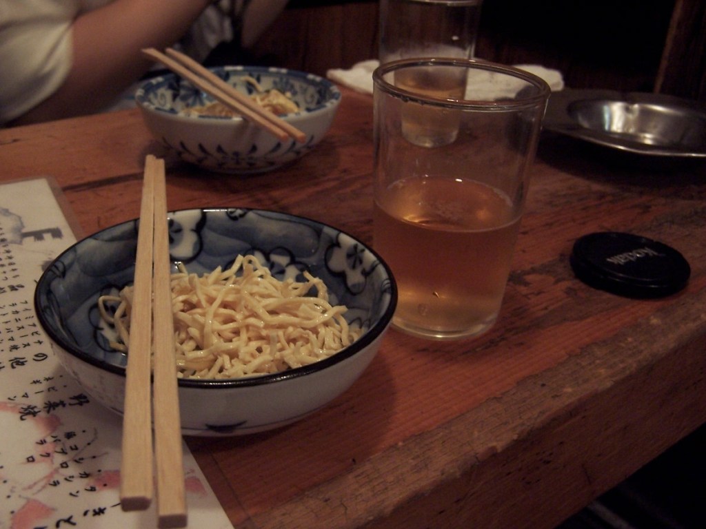 A cold glass of Japanese beer next to a small bowl of simple side dishes and wooden chopsticks