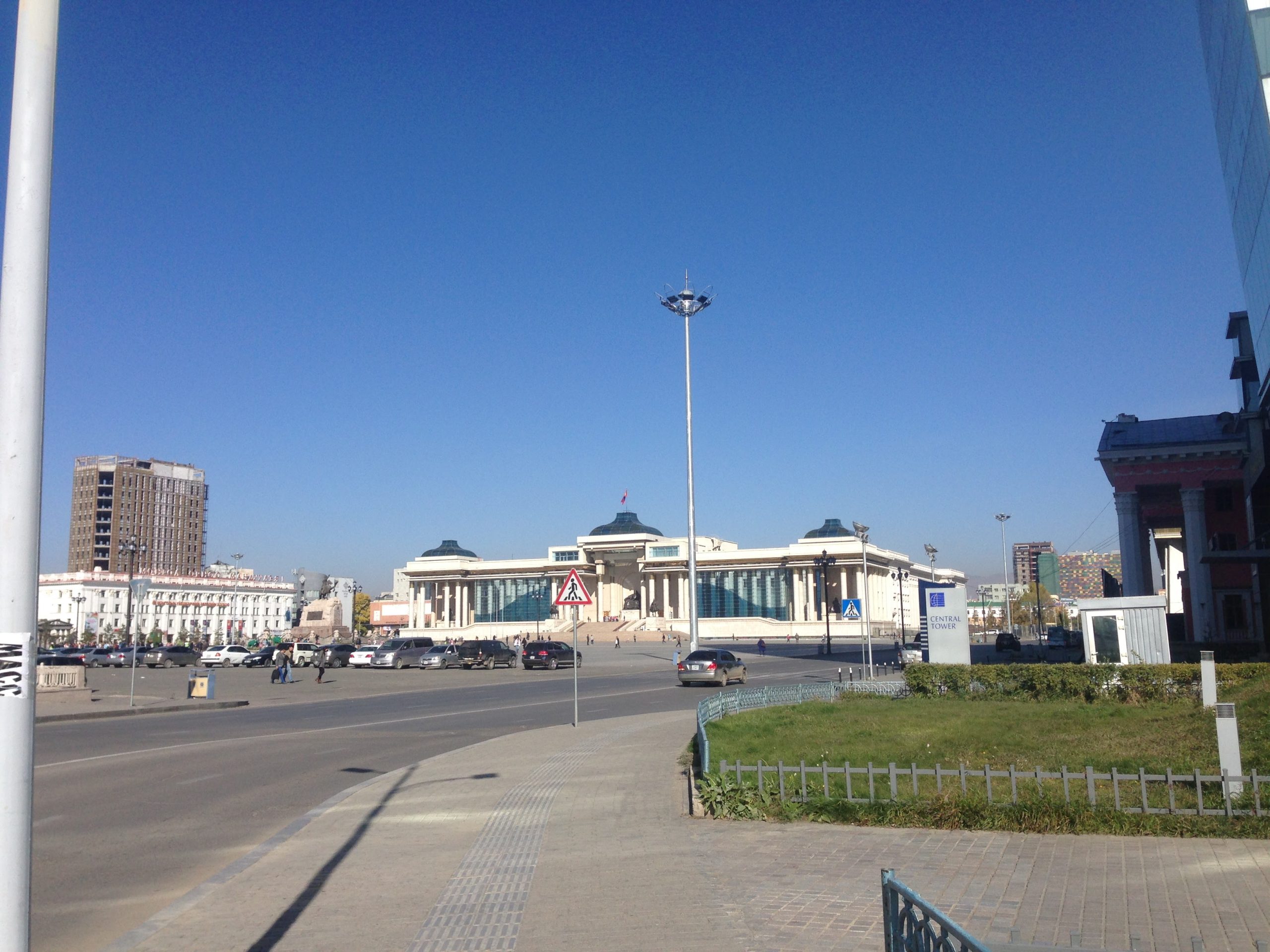 A wide-angle view of Sukhbaatar Square in Ulaanbaatar, Mongolia, under a perfectly clear and piercing blue autumn sky, with city buildings framing the edges.