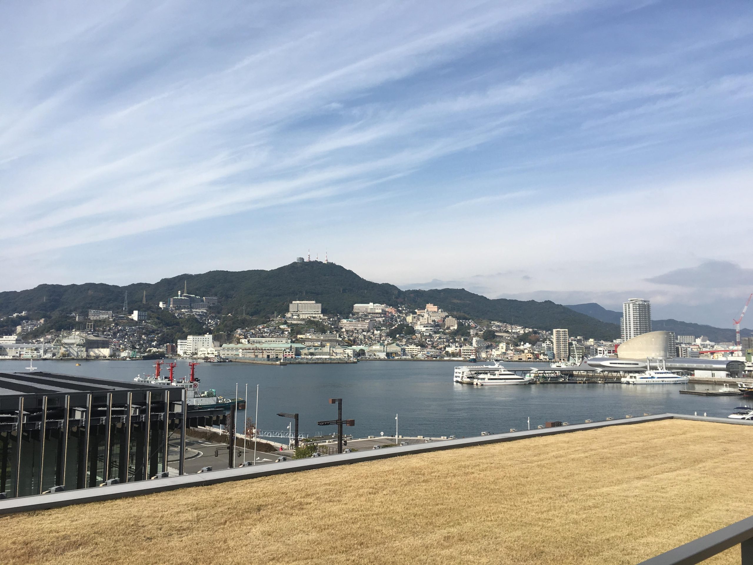 Rooftop view from Nagasaki Prefectural Art Museum overlooking Nagasaki harbor, moored ships, and hillside homes