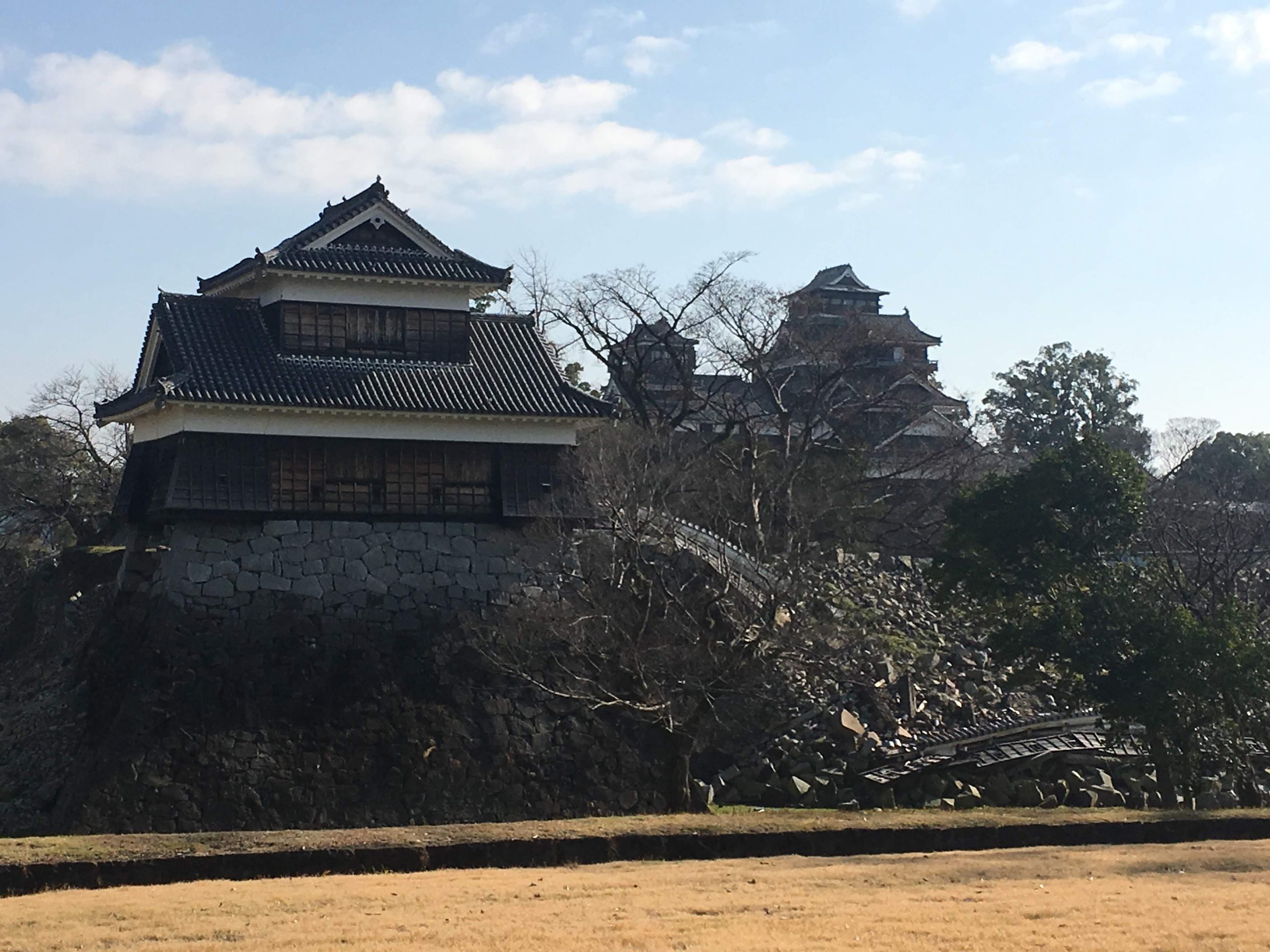 Massive, slumped stone walls at Kumamoto Castle showing visible earthquake destruction beneath the restored dark wooden structures.