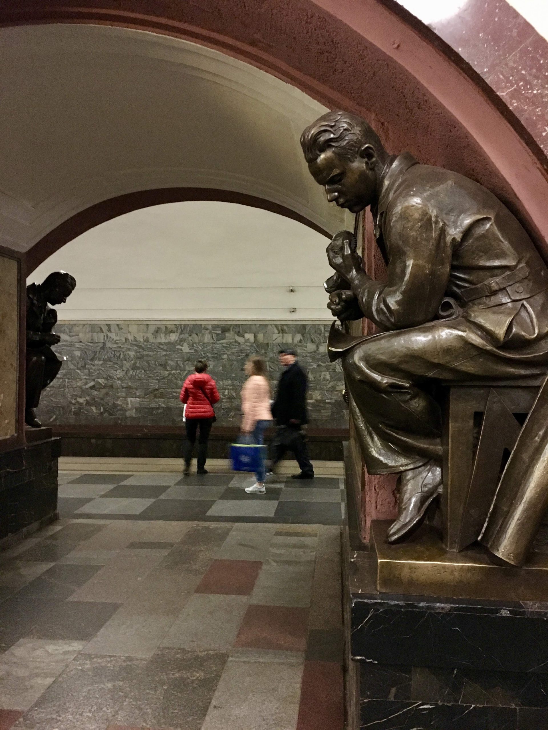 Deep red marble arches in Ploshchad Revolyutsii station, each flanked by detailed bronze sculptures of Soviet figures like workers and soldiers.
